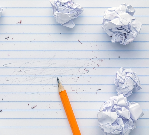 A yellow pencil on a sheet of lined notepaper, with erased-out writing and several crumpled balls of paper
