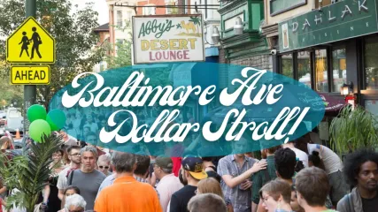 Image of people walking on Baltimore Avenue Dollar Stroll. White text framed in a transparent blue bubble, on top of image. Texts says " Baltimore Ave Dollar Stroll"