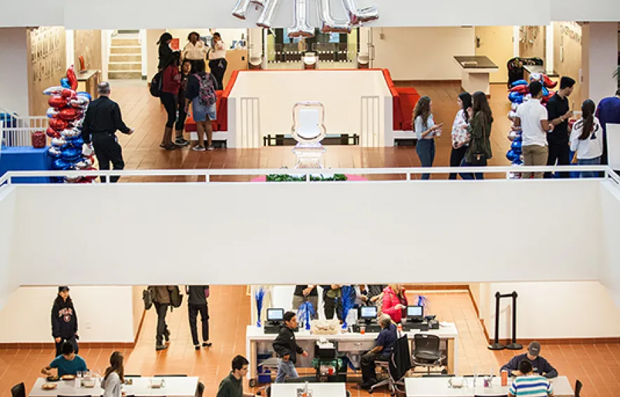 A view of Hill's atrium, showing students in the lobby level and on the dining level, with silver balloons spelling out "HILL"