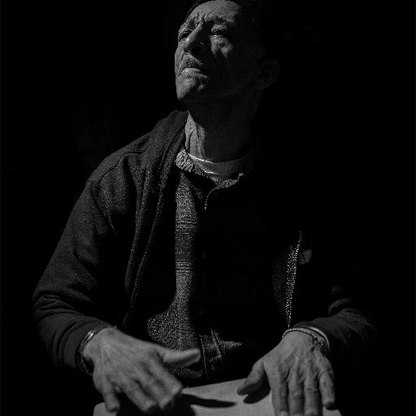 A black-and-white photo of a man drumming his hands on a flat piece of wood