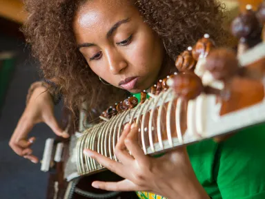 A young woman plays a sitar at a College House event.