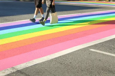 Two people walking in a crosswalk painted in the colors of the LGBTQIA+ flag